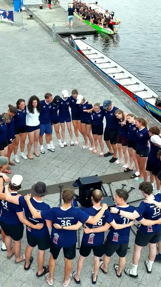 Teams stehen Arm in Arm im Kreis am Hafen